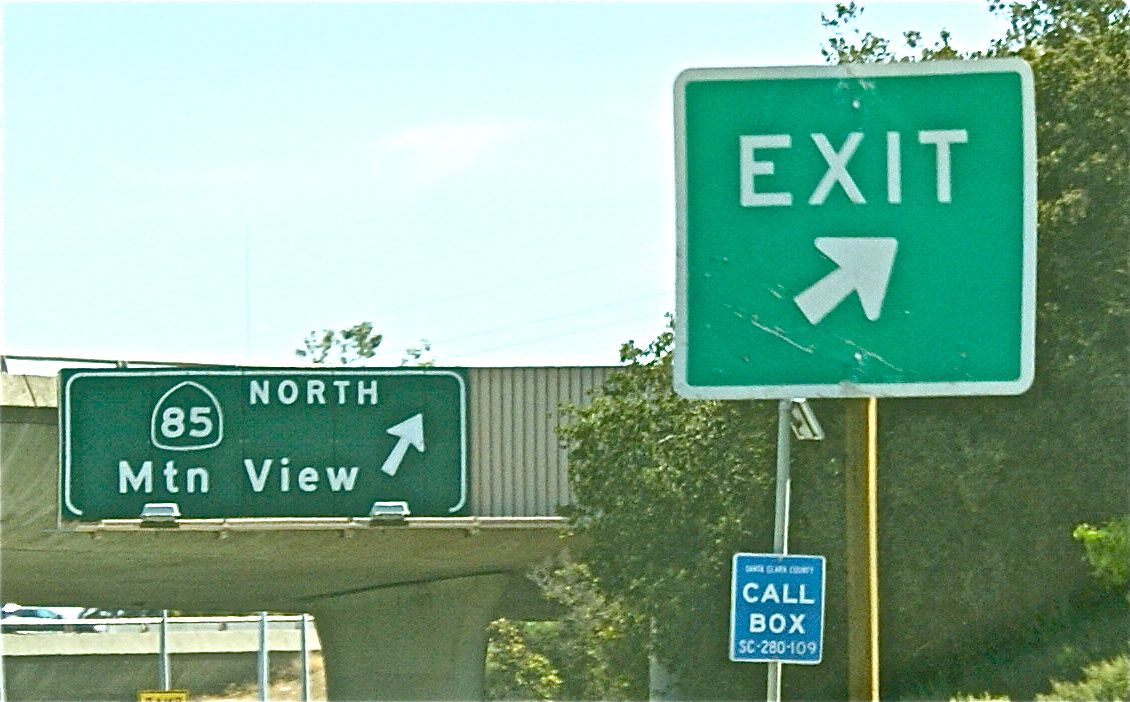 an exit sign and a highway sign near two road sides