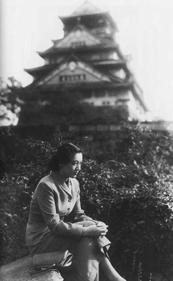 woman sitting on top of a big rock in front of a building