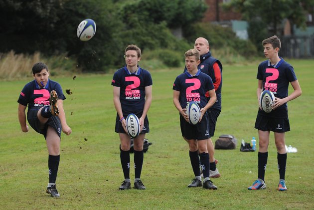 a group of young men standing next to each other holding onto rugby balls
