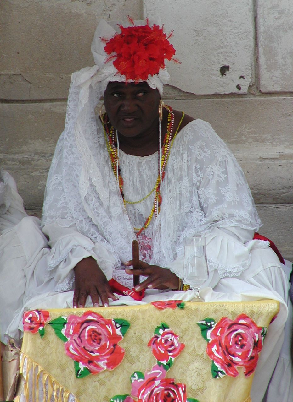 a man in a white dress sits at a table with red flowers
