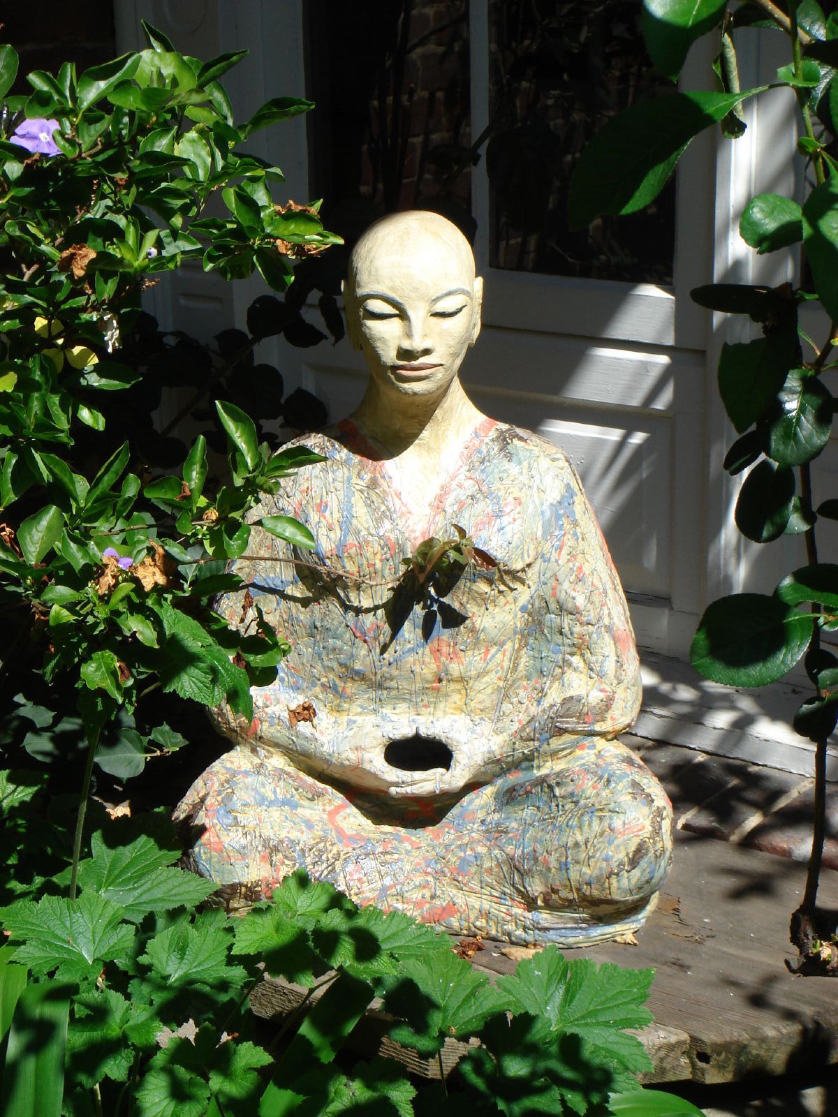 a statue of buddha sitting on top of a small statue in front of some flowers