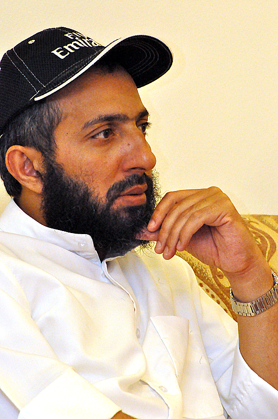 a man sitting down wearing a white shirt and black hat