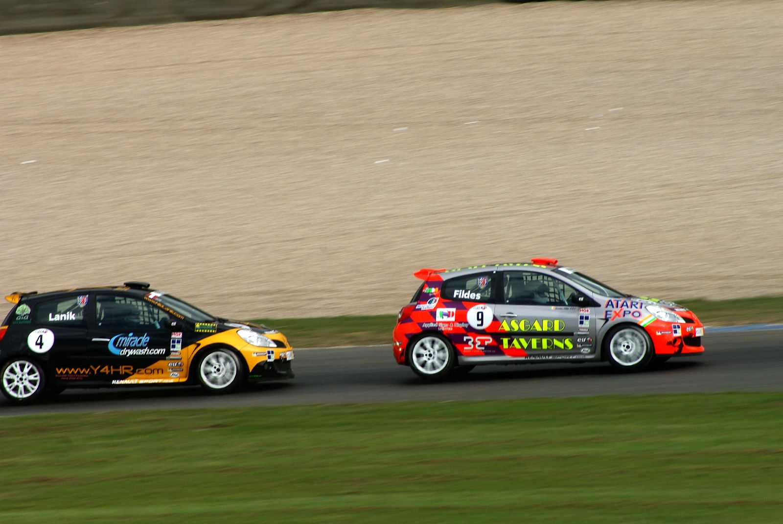 two racing cars one has red, the other black, at an angle of driving on a track