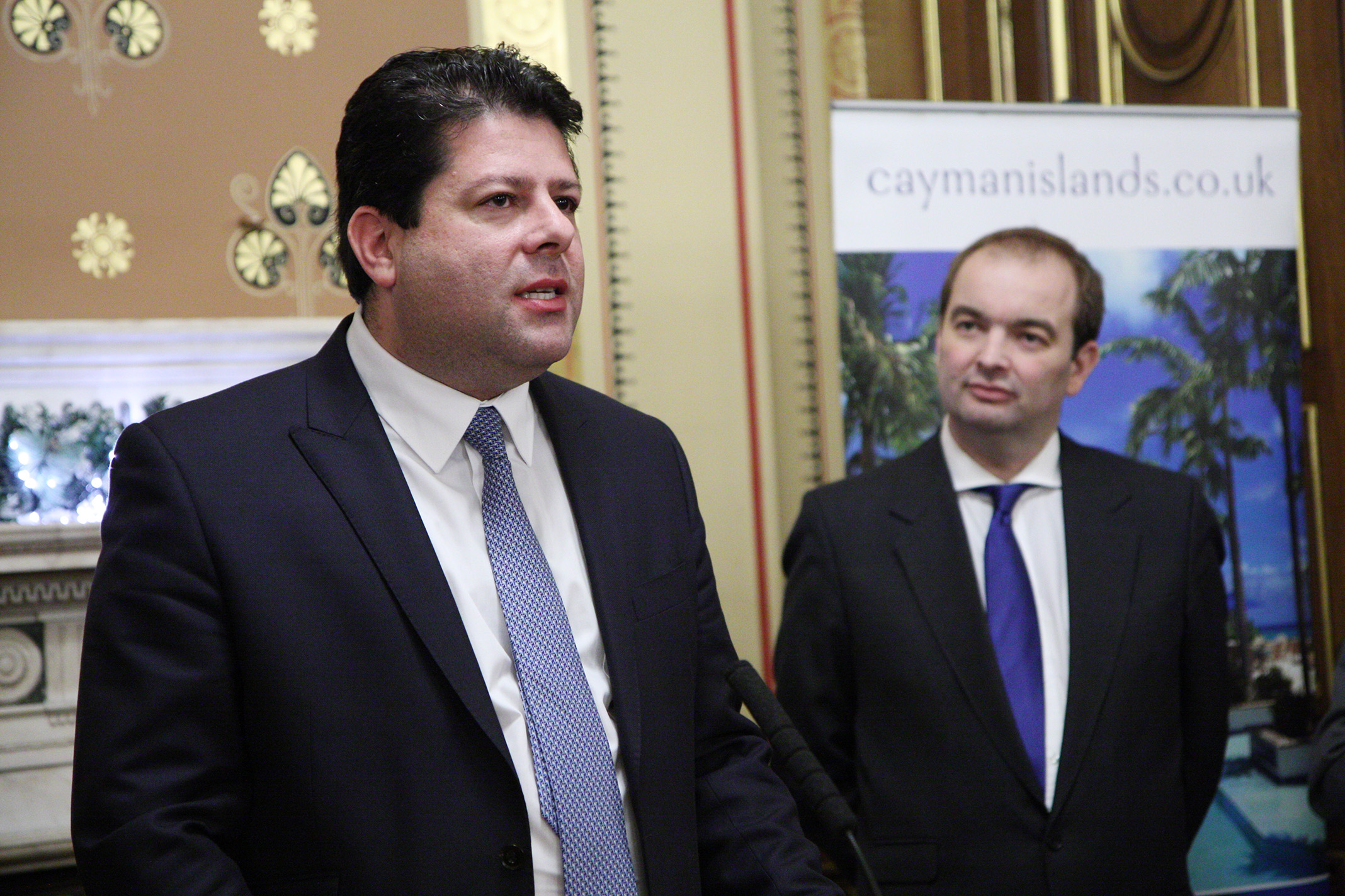 two men wearing suits standing in front of a large poster