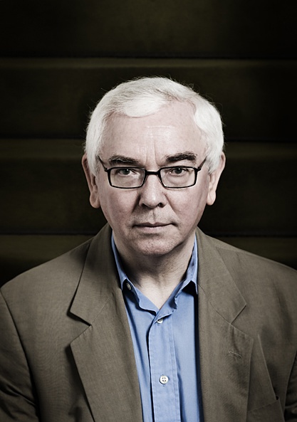 a white haired man in glasses sitting by a staircase