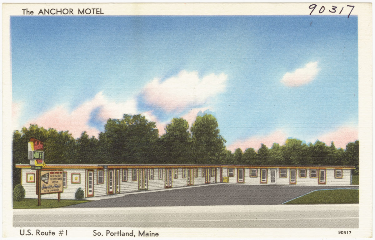 a motel building with the parking lot and trees in the foreground