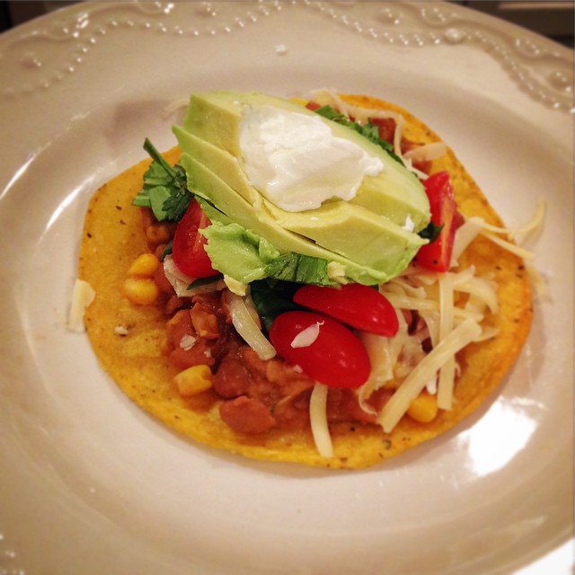 an open - faced plate holds a tortilla topped with salsa, avocado, and shredded cheese