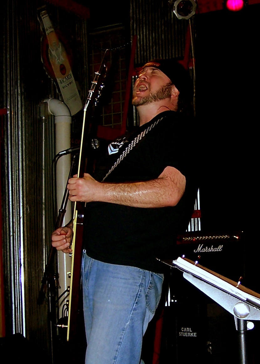 a man holding a long guitar while standing in front of a microphone
