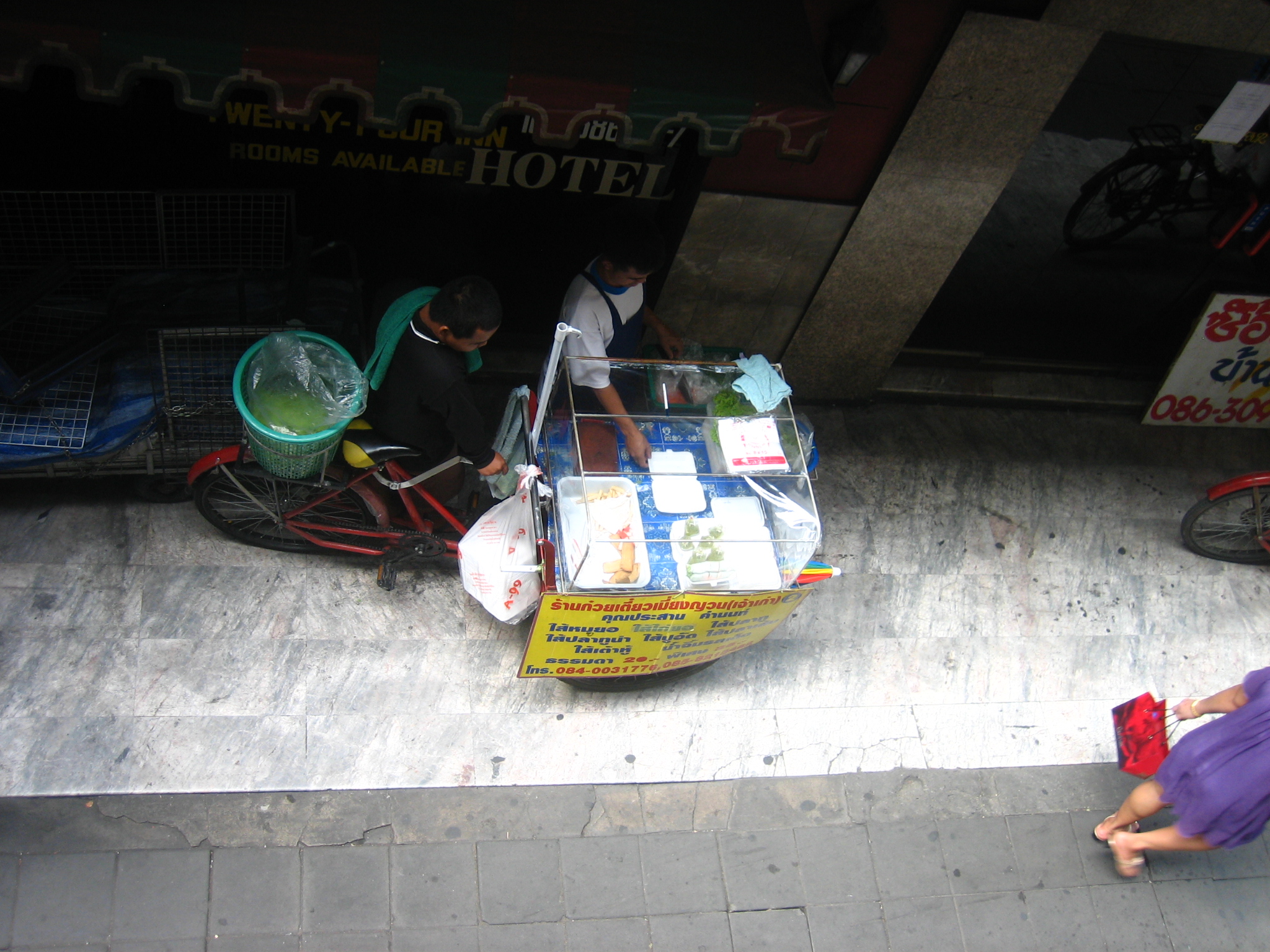 three people are walking near a cart with several containers on top