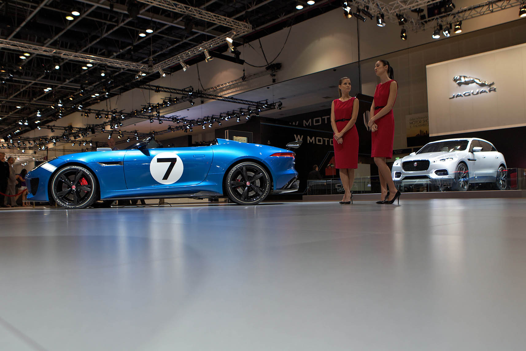 two women in red dresses stand next to the new jaguar car