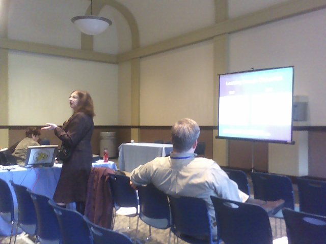 a woman talking in front of a room full of people