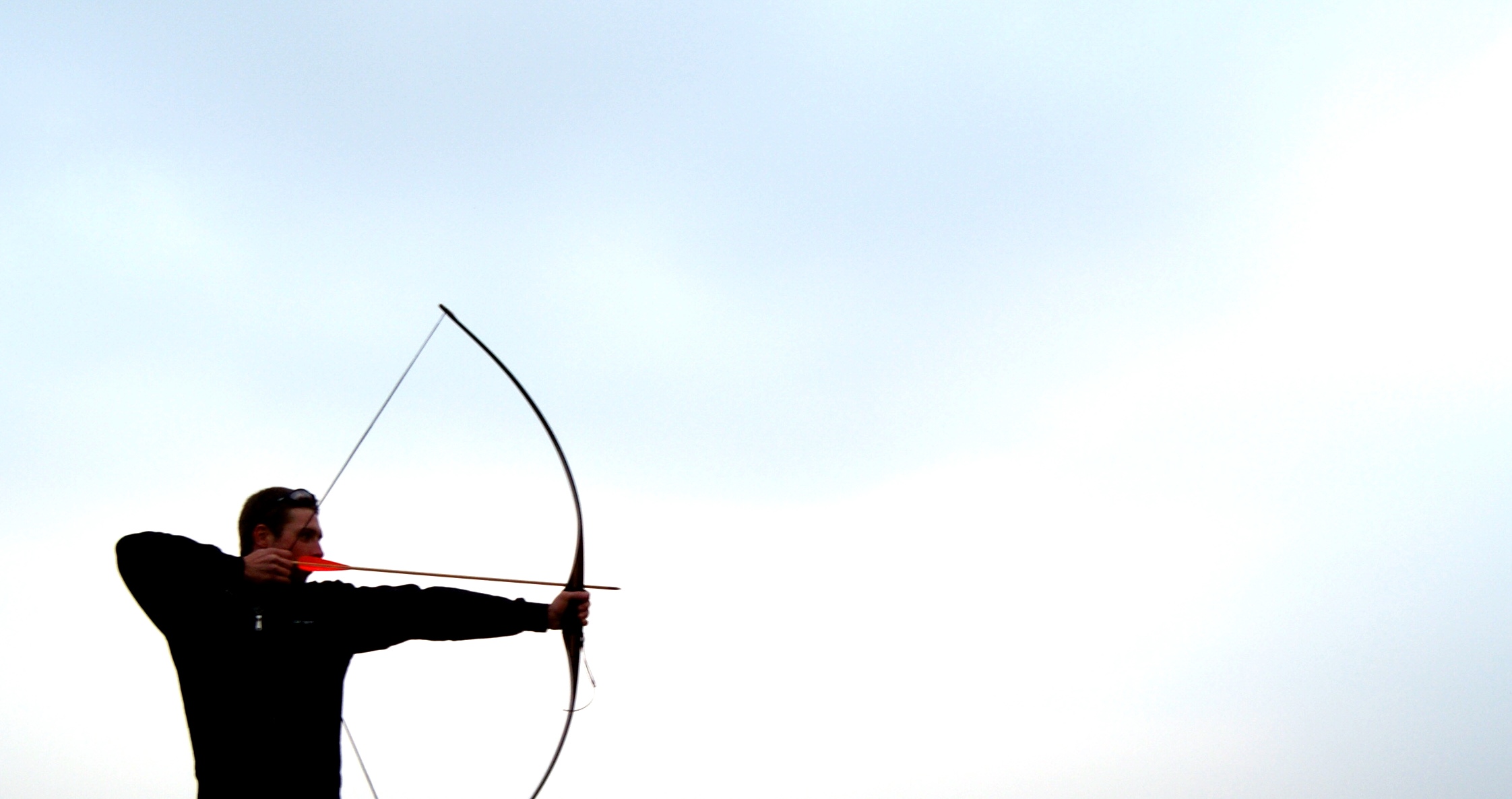 man with bow and arrow on open range shooting