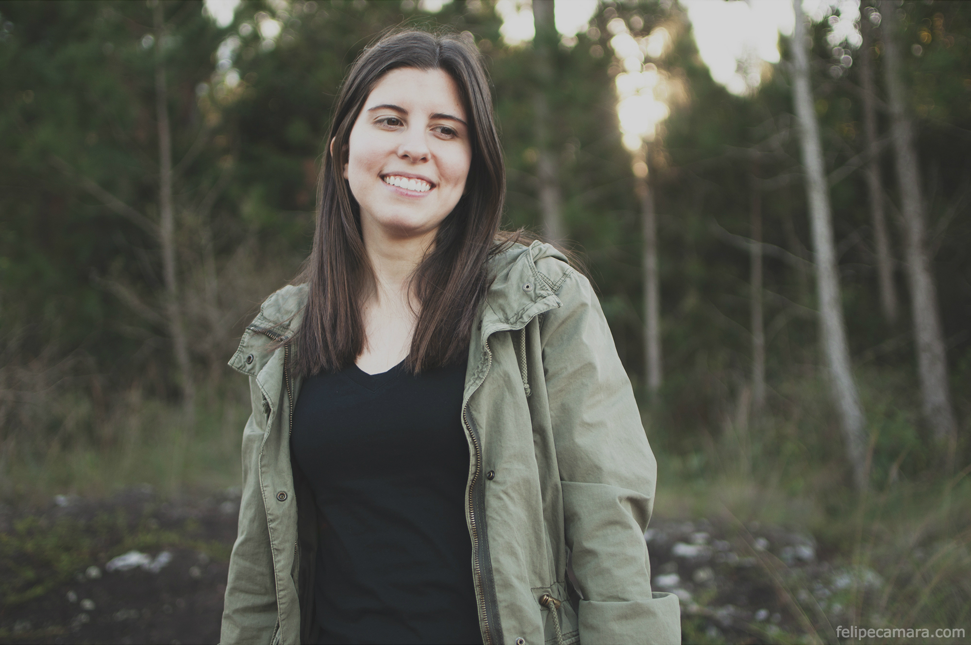 a woman standing in the woods smiling for a picture