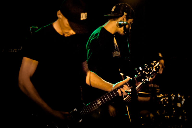 two men holding guitars together while playing on a dark stage