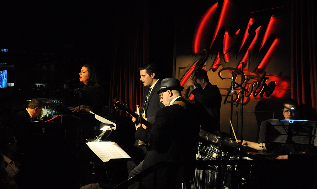 a conductor, bandleader and musicians in dark lighting with signs in background