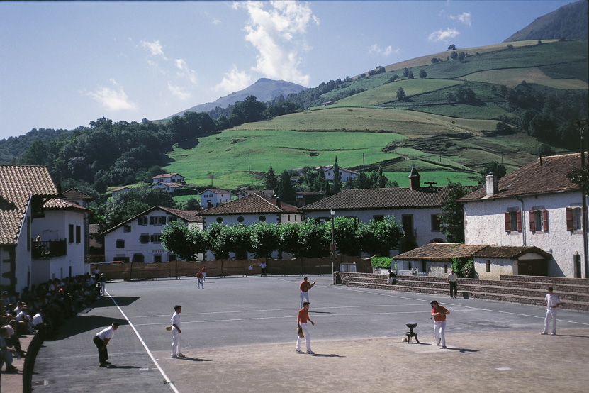 people playing tennis in an asphalt court outside a town