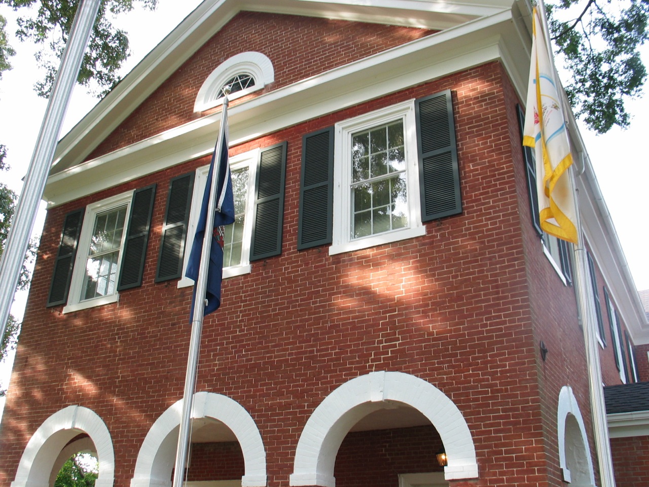 a red brick house has two flags on the outside and three blue and white flags in front of it