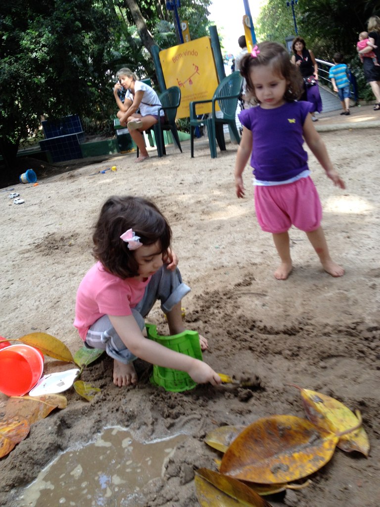 two young children playing in sand with fake leaves