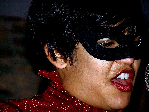 an asian woman with a mask singing into a microphone