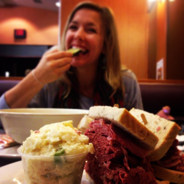 woman eating sandwich and cole slaw with a side of potatoes