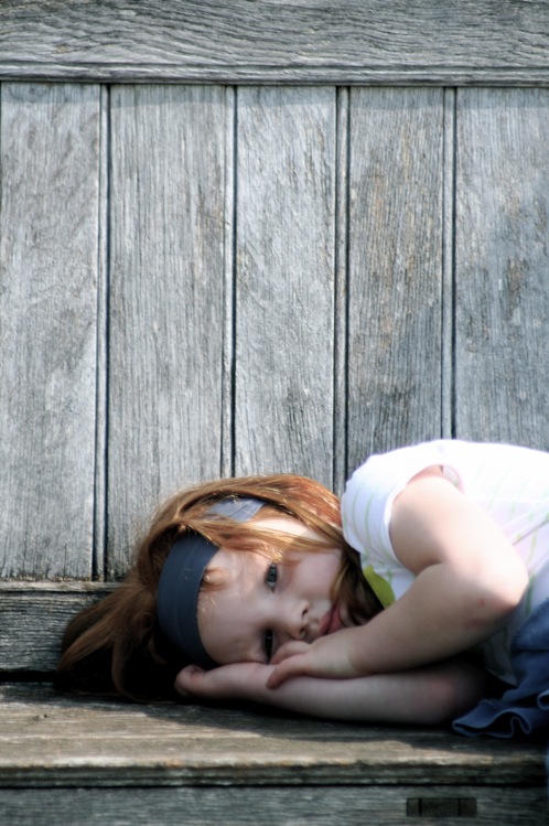 a small girl is laying down on a bench