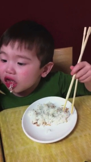 the small child is eating rice with chopsticks