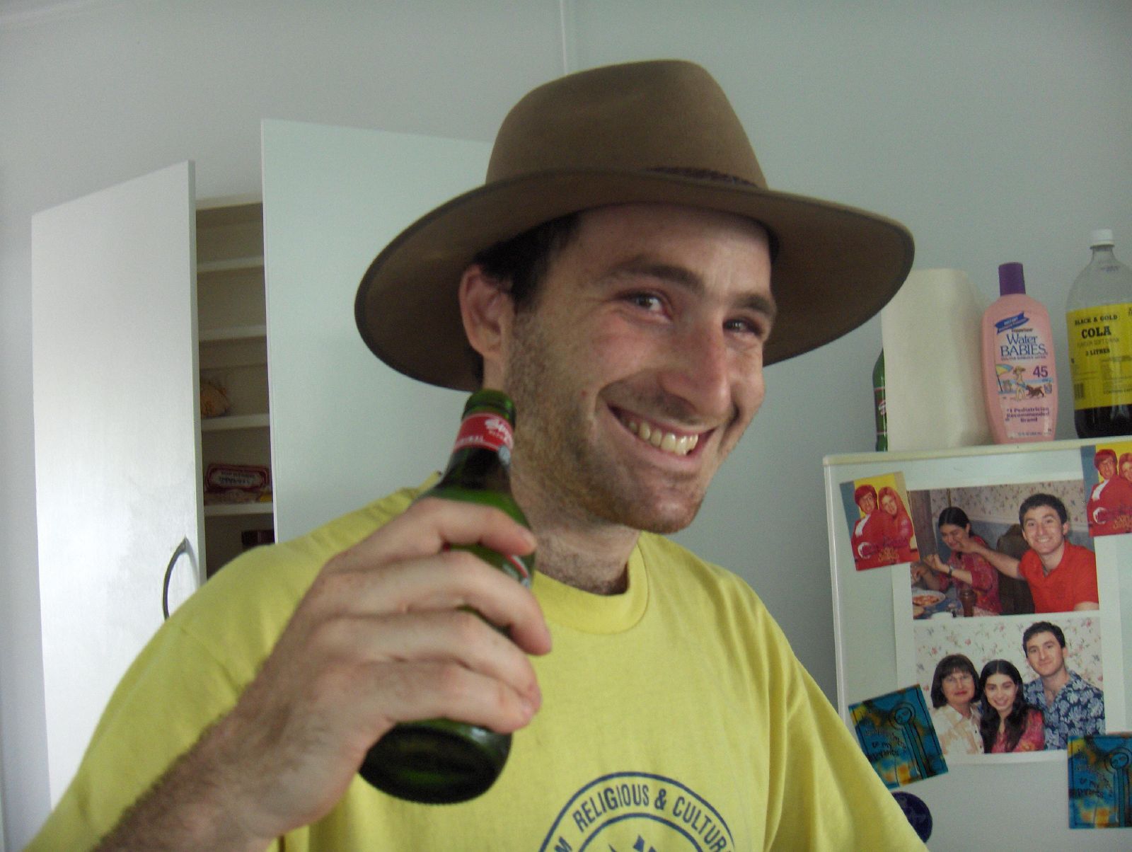 a man wearing a yellow shirt and hat is holding up a bottle