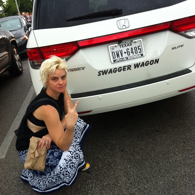 woman sitting on the ground near a white van and giving peace sign