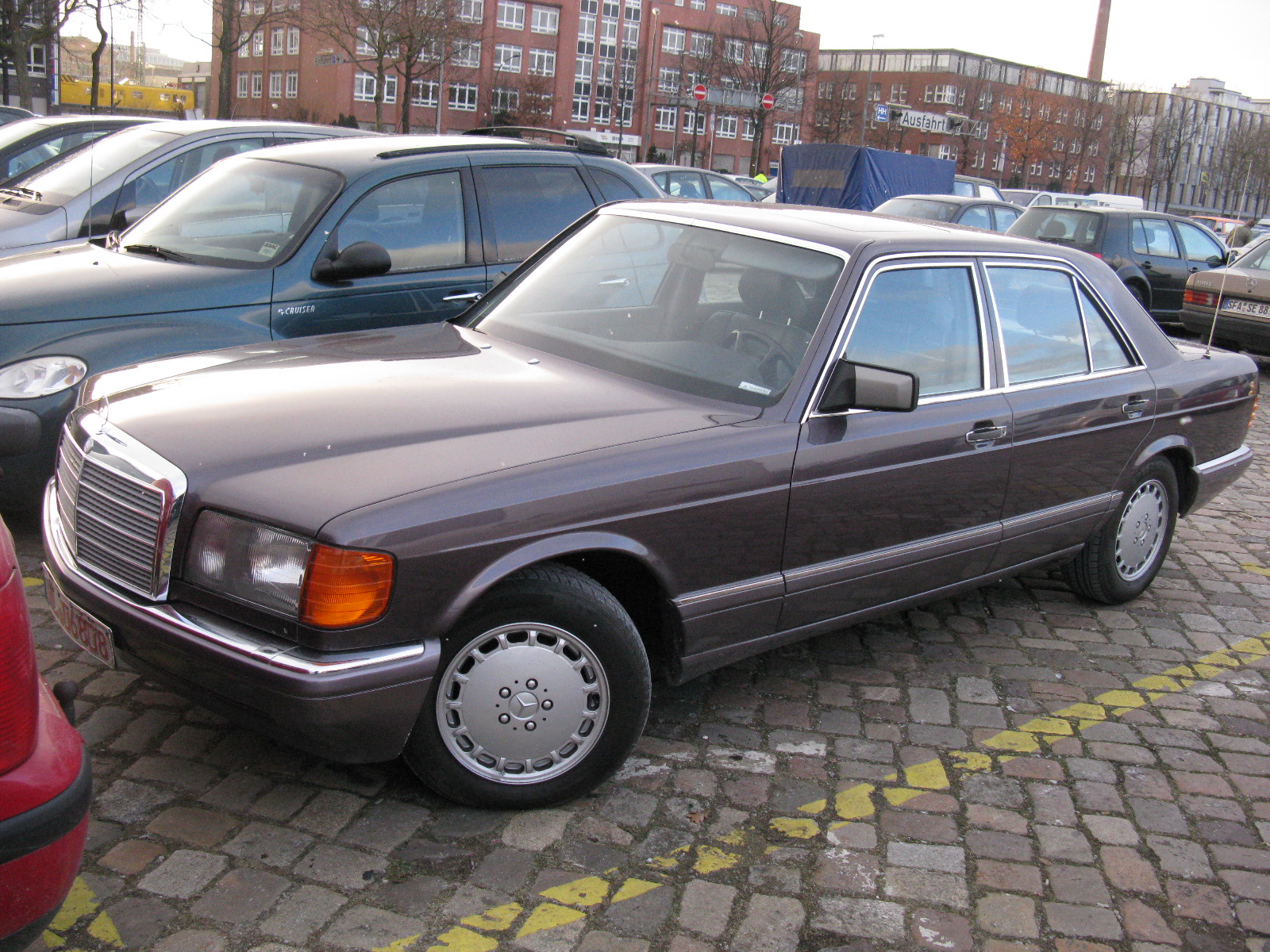 a large brown mercedes parked next to other cars