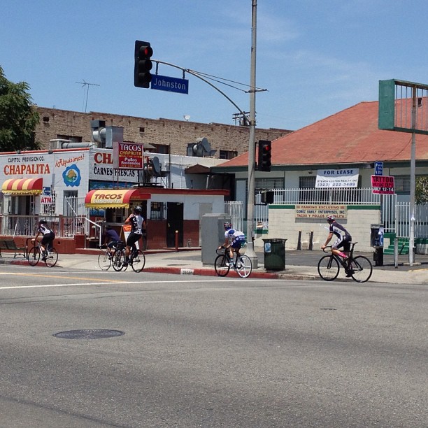 several bicyclists are riding by shops and traffic lights