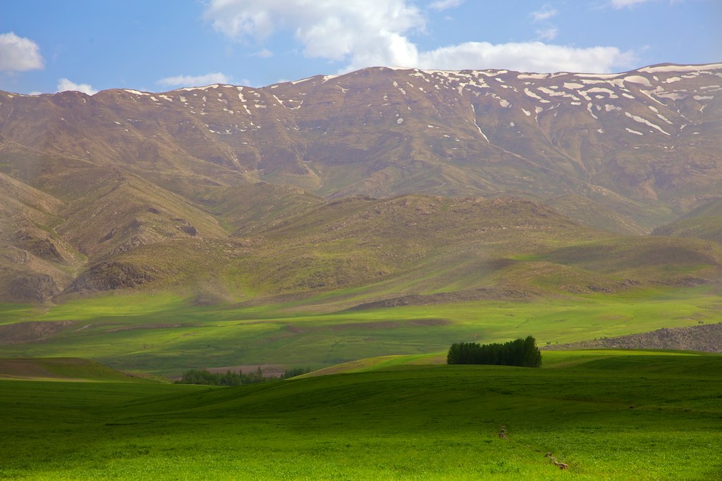 a green pasture in front of mountains and clouds