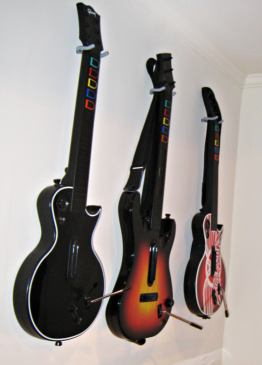three guitars hang on a wall above two other guitars
