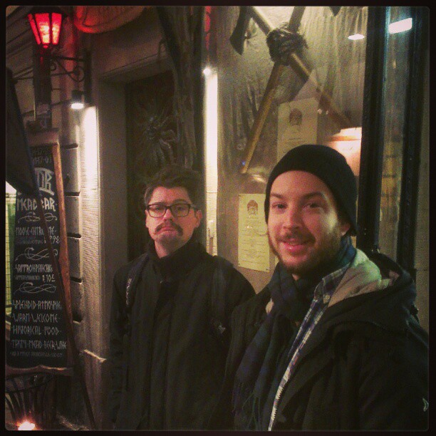 two men in winter clothes standing outside of a restaurant