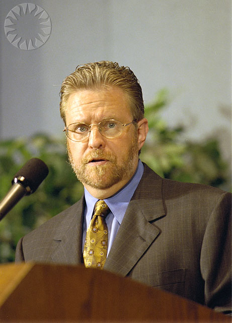 a man wearing glasses and a tie in front of a microphone
