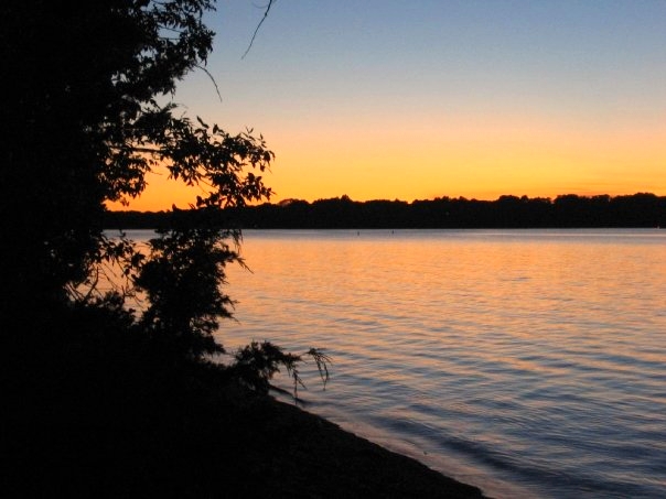 a sunset is shown over the water with a tree line