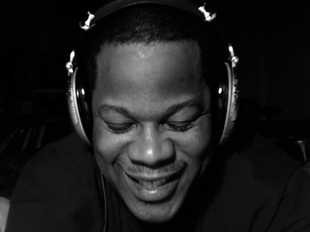 a man wearing a pair of headphones smiles and looks down