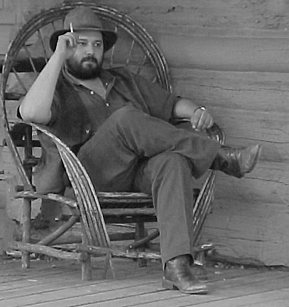 a bearded man in a cowboy hat is sitting in a chair on the porch