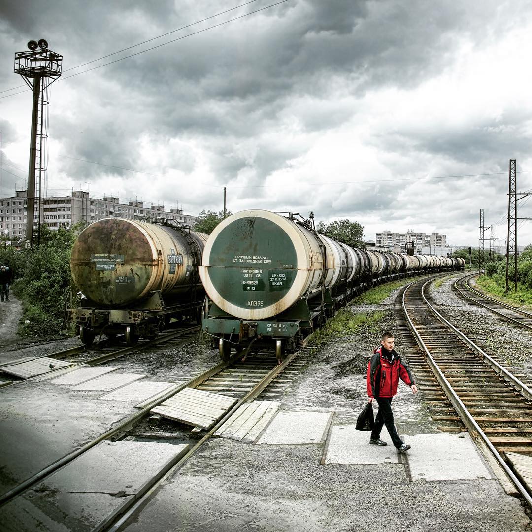a man in a red coat walks past oil tanks on the tracks