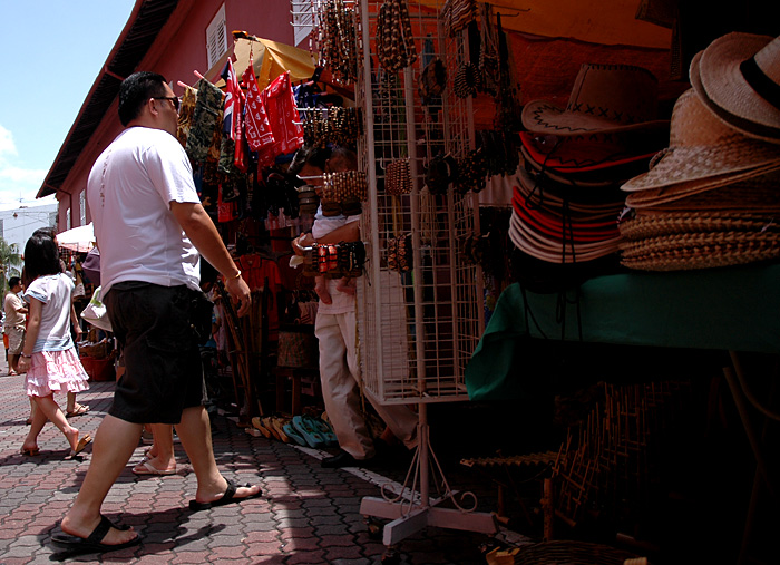 a man walking past a store selling handbags and hats