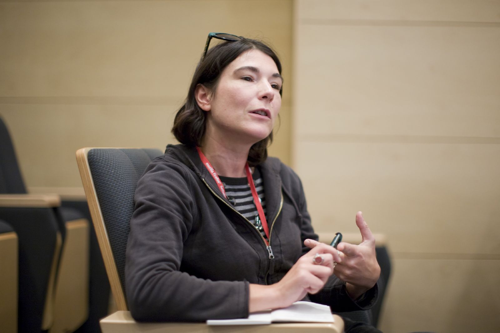 a woman in glasses sits at a table speaking