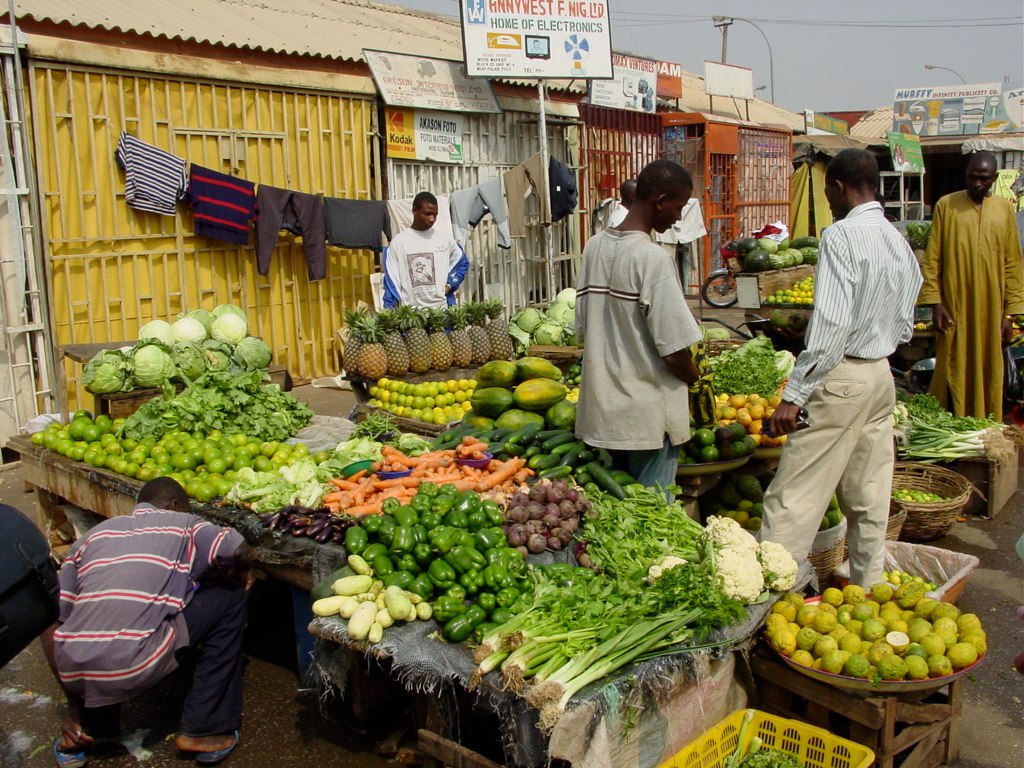several people standing around a fruit and vegetable stand