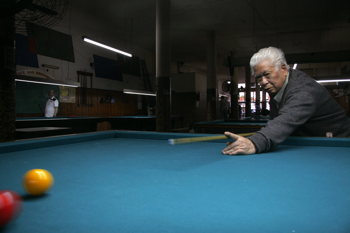 an older man leaning over and reaching down to hit a pool ball