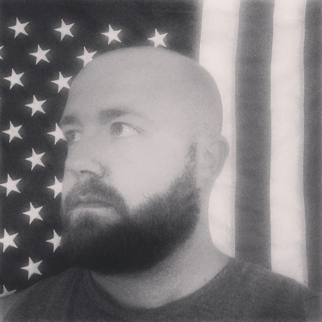 a man with a bald head standing next to a flag