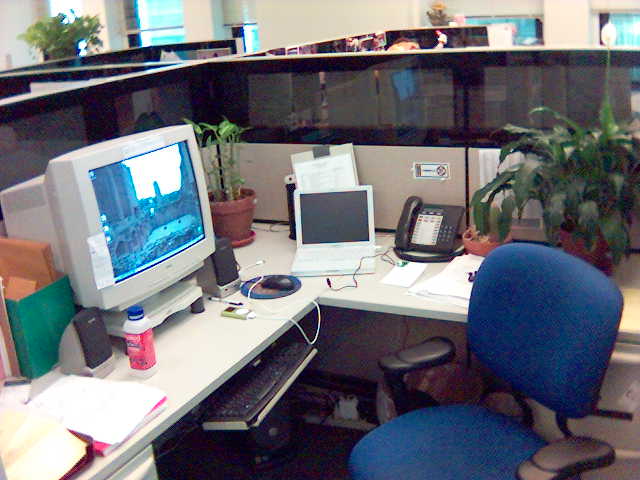 an office cubicle with two desk chairs, monitors, a phone, and a computer