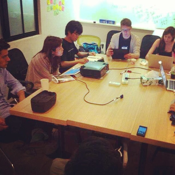 a group of people sit at a table working on electronic devices