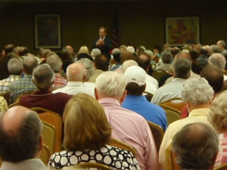 an audience in a conference room watching a person on a stage