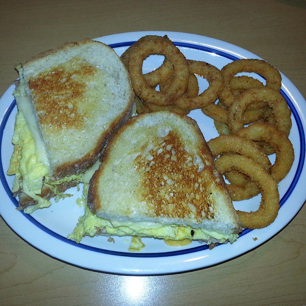 a grilled cheese sandwich with an egg, melted cheese and onion rings