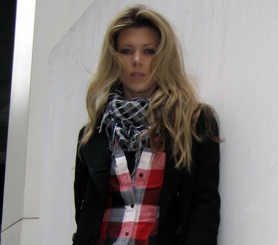 woman leaning on wall with hands in pockets wearing plaid scarf