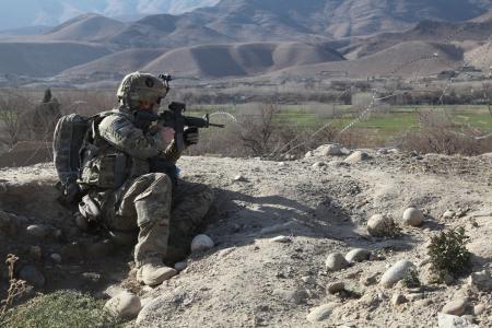 a soldier kneeling on the side of a hill, with his gun in hand