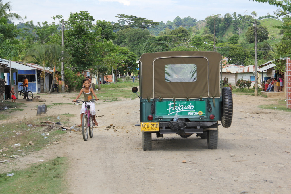 a green vehicle with a person riding it down a dirt road